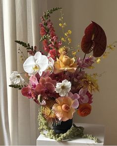 a vase filled with lots of colorful flowers on top of a white table next to a window