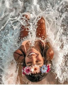 a woman laying on top of the ocean with flowers in her hair