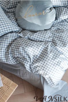 a bed with blue and white checkered comforter on it, next to a wicker basket