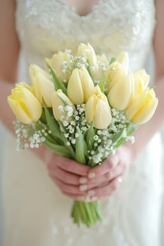 a bride holding a bouquet of yellow tulips and baby's breath flowers