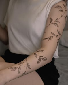 a woman's arm with leaves on it and a white t - shirt in the background