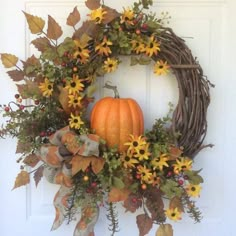 a wreath with sunflowers and leaves is hanging on the front door, next to a pumpkin