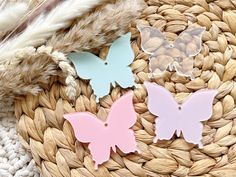 three pastel butterflies sitting on top of a woven basket next to some dried feathers