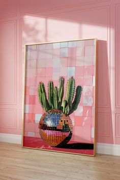 a cactus in a mosaic vase against a pink wall with wood floor and wooden frame