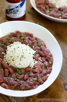 two white bowls filled with beans and rice on top of a wooden table next to a jar of ketchup