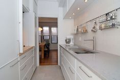 a narrow kitchen with white cabinets and counter tops