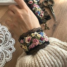 a woman's hand wearing a black lace bracelet with colorful flowers on it next to scissors