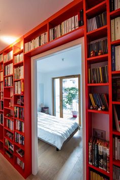 a bedroom with red bookshelves and a bed in the middle is seen through an open door