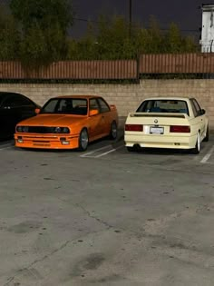 three cars parked in a parking lot next to a brick wall and fence at night