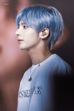 a young man with blue hair and piercings on his ears looking off to the side