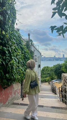 an older woman walking down the sidewalk near some trees and water in the distance, with a city skyline behind her