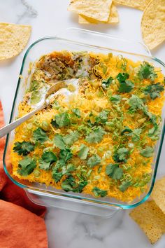 a glass casserole dish filled with cheese, cilantro and tortilla chips