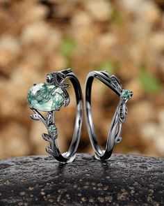 two wedding rings with green stones and leaves on top of each other, sitting on a rock