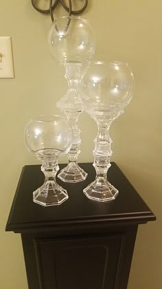 three clear glass goblets sitting on top of a black table next to a pair of glasses