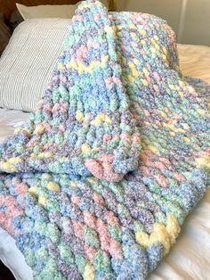 a crocheted blanket sitting on top of a bed next to a striped pillow