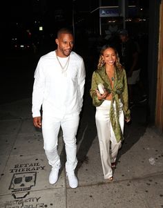 a man and woman are walking down the street at night, one is wearing white