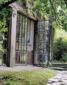 an old building with glass doors and stone steps leading up to the front door is surrounded by greenery