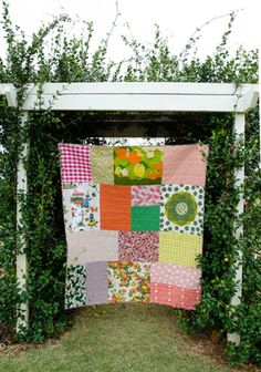 a patchwork quilt hanging from a white pergolated trellis in front of an arbor