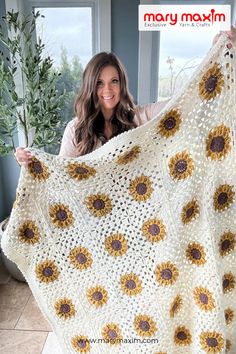 a woman holding up a crocheted sunflower blanket