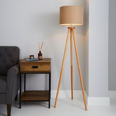 a wooden tripod floor lamp next to a gray chair and end table with a light on it