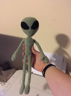 a hand holding a small green crocheted alien doll with black eyes and nose