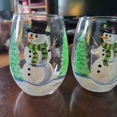 two wine glasses with snowmen painted on them sitting on top of a wooden table