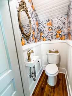 a white toilet sitting inside of a bathroom next to a sink and wooden flooring