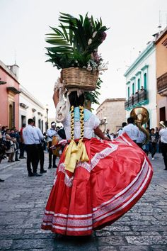 a woman in a red and white dress carrying a basket with flowers on her head