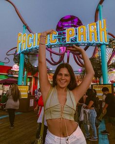 a woman holding up a sign that says pacific park in front of an amusement park