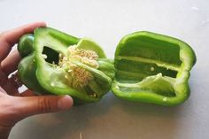 a person is holding an open green bell pepper on a white counter top, with the end cut off