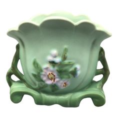 a green vase with flowers on it sitting in front of a white background and the bottom is empty