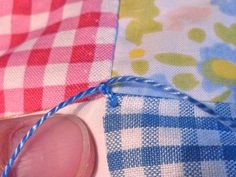 someone is stitching together fabric with a blue string on the end and another piece of material in the background