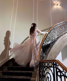 a woman in a long white dress is walking down the stairs with her arms outstretched