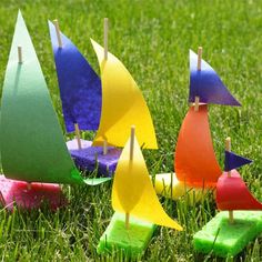 small boats made out of paper sitting in the grass with clothes pins stuck to them