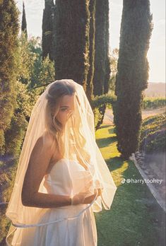 a woman in a wedding dress is holding a white veil over her head and looking at the camera