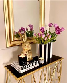 a black and gold console table with pink flowers in vases next to a mirror