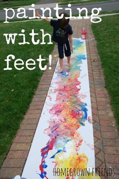 a young boy is painting on the sidewalk with his feet and hand painted rainbow colors