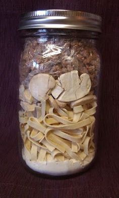 a jar filled with pasta and mushrooms on top of a wooden table next to a purple cloth