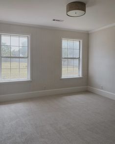 an empty room with two windows and carpet