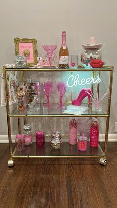 a gold bar cart filled with lots of pink and white items on top of a hard wood floor