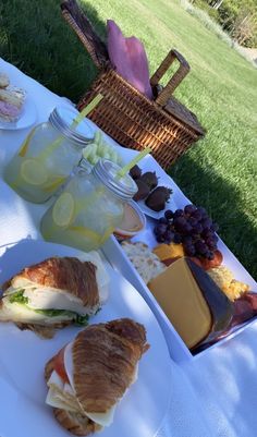 a table topped with sandwiches and drinks on top of a white cloth covered picnic table