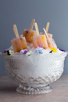 popsicles are arranged on top of ice in a glass bowl with flowers and daisies