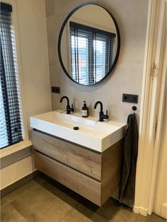 a white sink sitting under a round mirror next to a wooden cabinet with two faucets