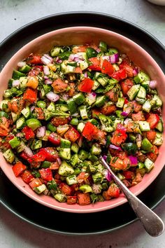 a pink bowl filled with chopped vegetables next to two glasses and spoons on a table