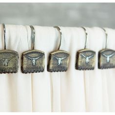 four metal hooks hang from the curtain in front of a white drapes with longhorns on them