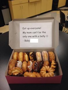 a box filled with lots of donuts sitting on top of a table next to a sign that says, eat up everyone my mom can't be the only one with a belly