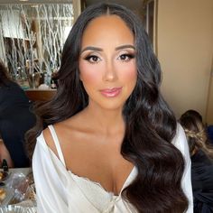 a woman with long dark hair wearing a white dress and posing in front of a table full of food