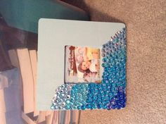 a photo frame with blue and silver beads on the bottom is sitting next to a stack of books