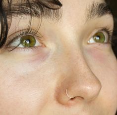 a close up of a woman's face with green eyes and nose piercings