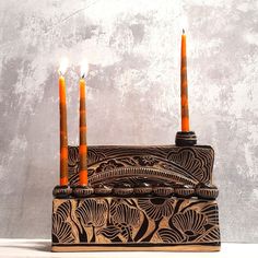 three candles are lit in a decorative box with intricate designs on the front and sides